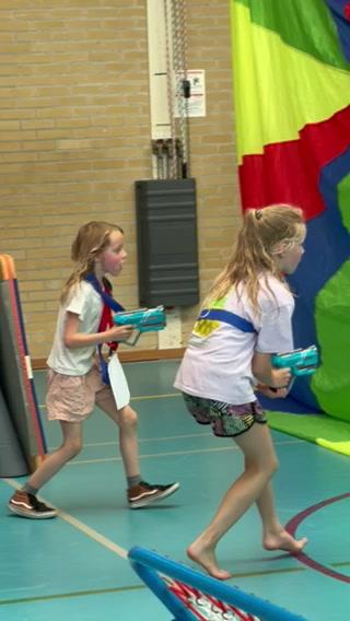 Two young girls playfully run in a gymnasium while holding toy guns